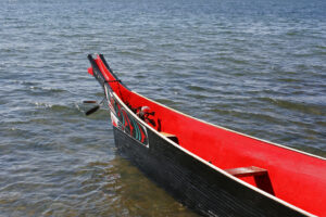 An empty Indigenous Boat with red paint interior sits on the water